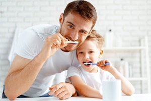 Father and son brushing teeth together in front of mirror