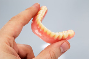 Person holding lower denture between thumb and forefinger