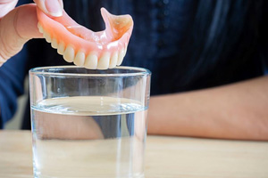 Hand placing denture in a cup of water