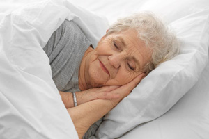 Senior woman sleeping peacefully in white bed linens