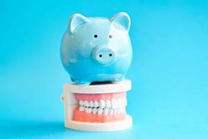Piggy bank atop model teeth representing the cost of dental emergencies in East Hartford