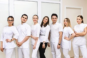 Dental team dressed in white, posing against neutral wall