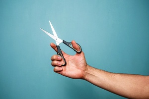 Man’s hand holding pair of scissors against teal background