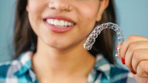 Person holding Invisalign aligner in front of her smile